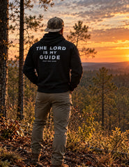 Man wearing the black The Lord Is My Guide® hoodie, back print, overlooking pine woods at sunset – Hunt One More