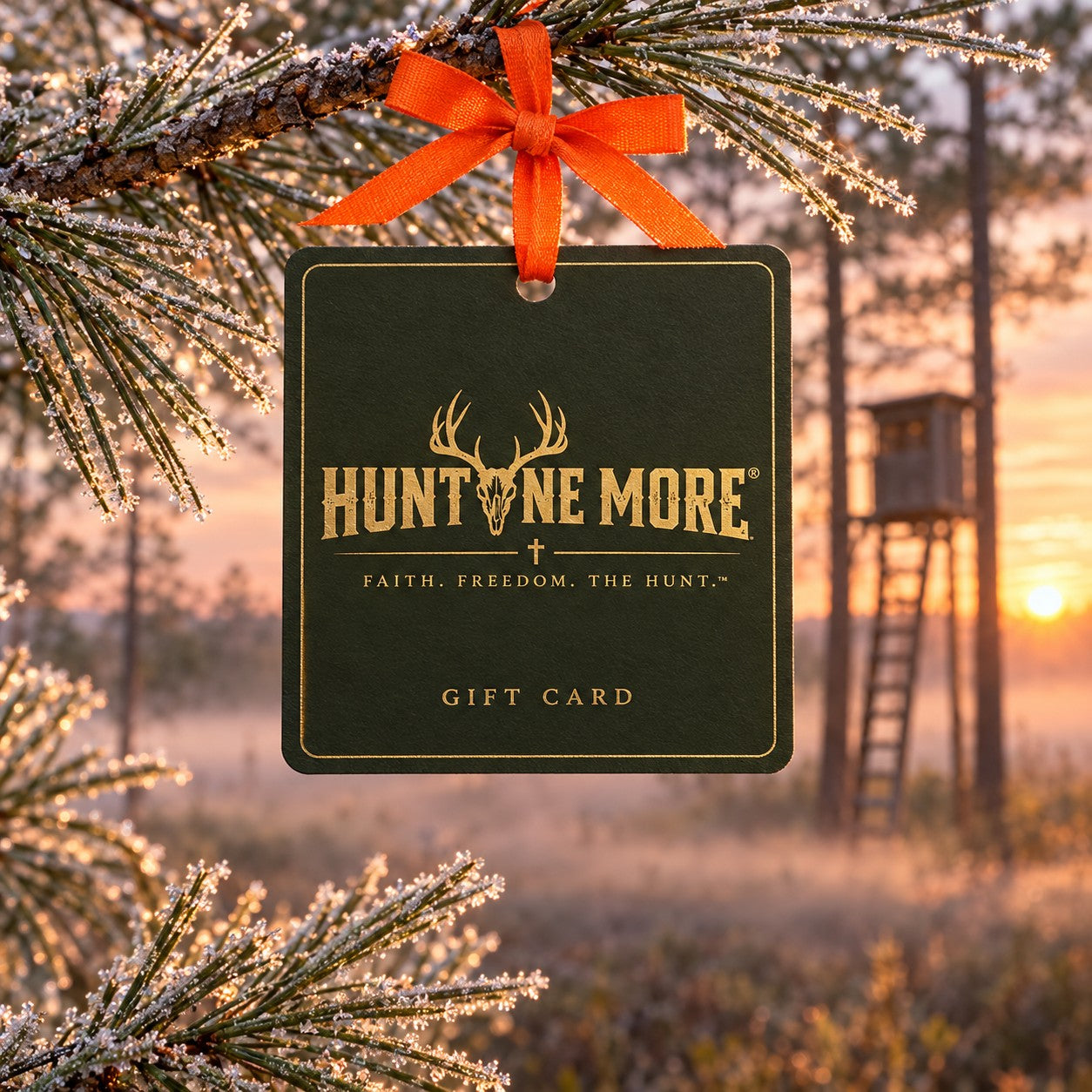 Hunt One More gift card hanging from a frosted pine branch with an orange ribbon at deer camp