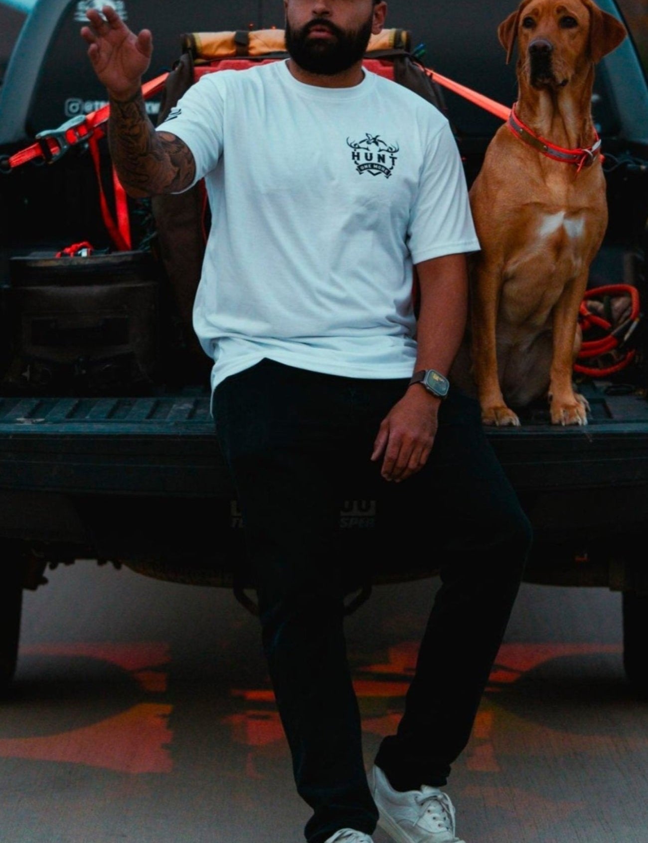 Man wearing the white Stripes and Antlers tee, sitting on a truck tailgate with his dog
