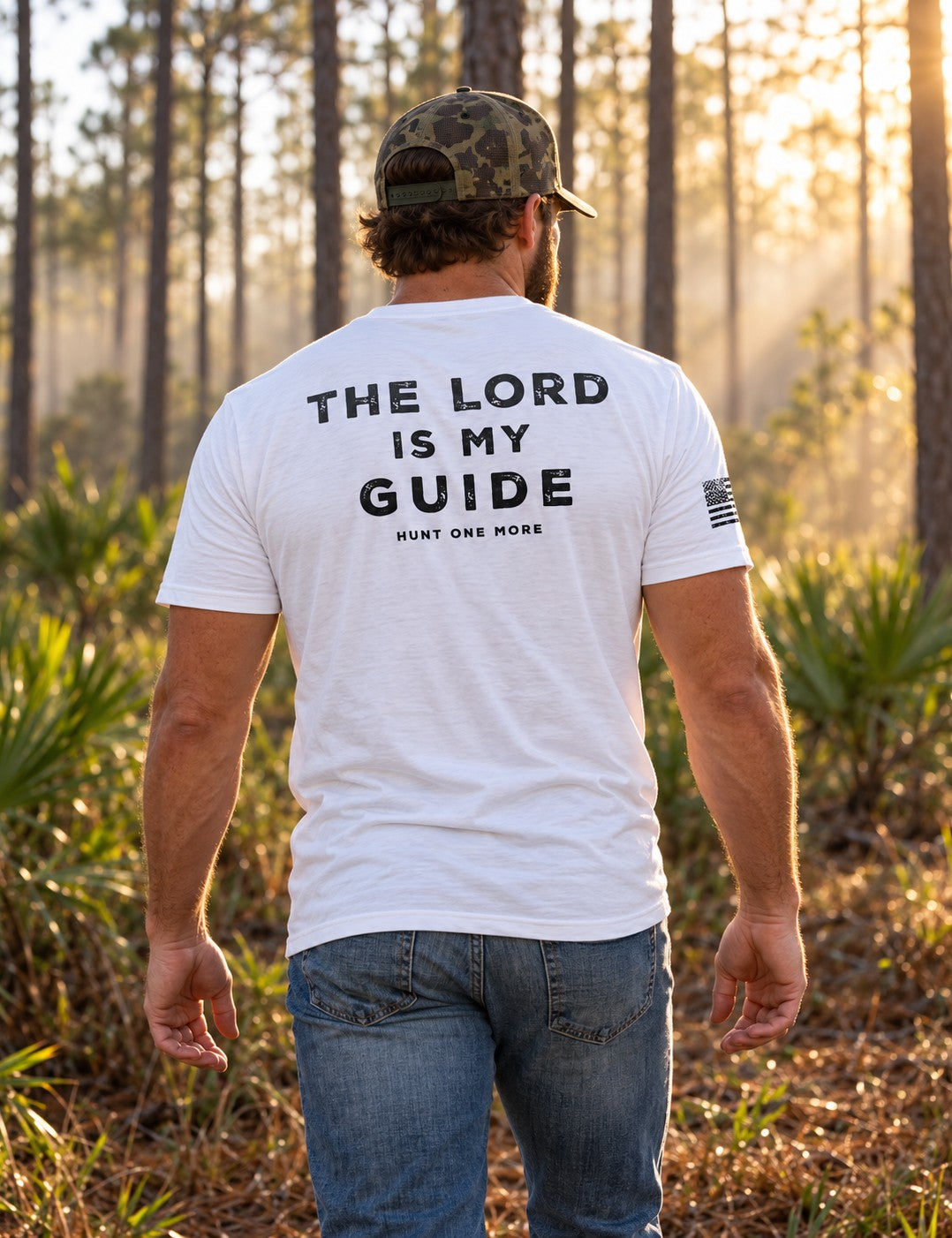 Man wearing the white The Lord Is My Guide® tee, navy back print, walking through a misty pine forest at sunrise – Hunt One More